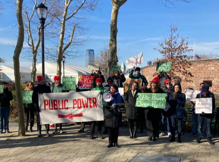 Line of demostrators facing the camera, dressed for cold morning, holding signs reading 